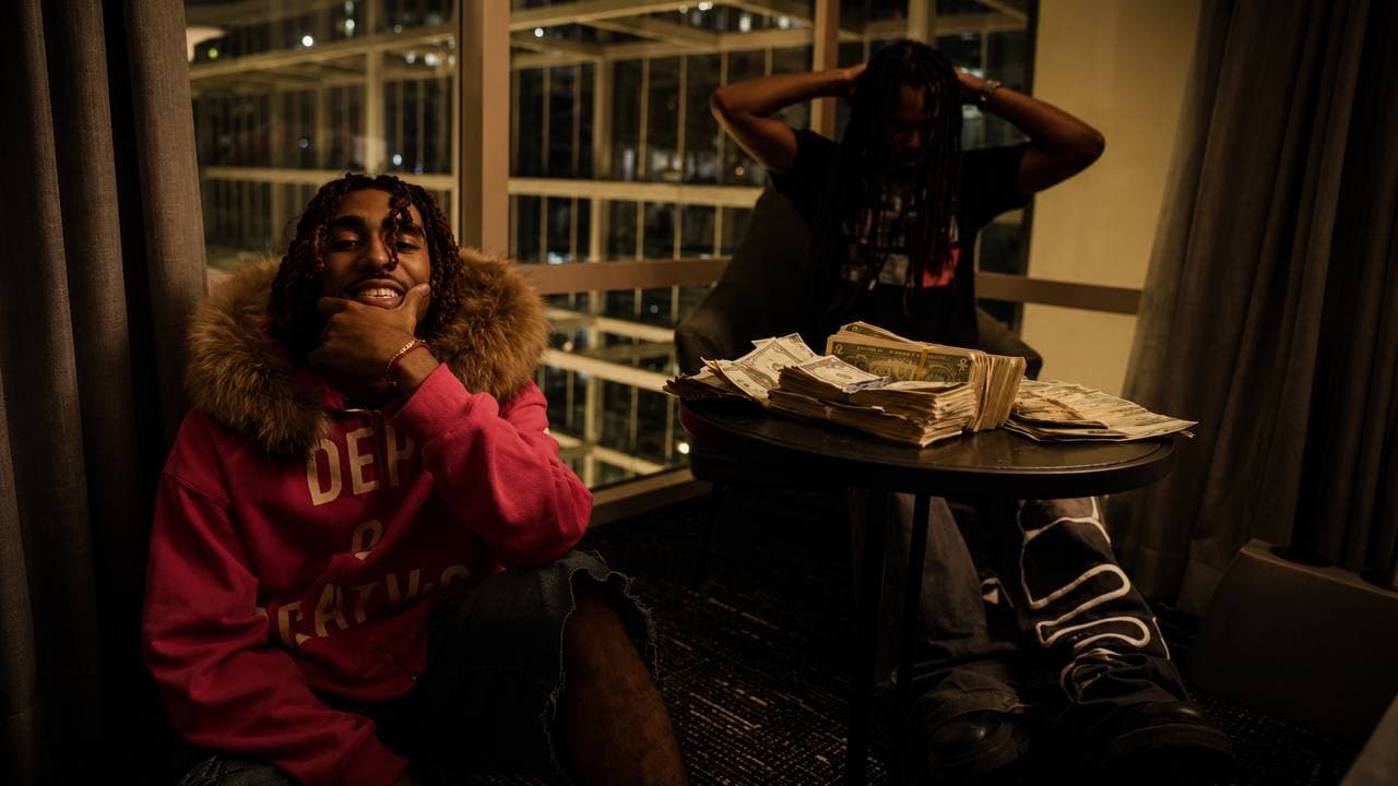 Luxury Bran editorial photograph with a creator in a pink hoodie seated beside a table in a city apartment.